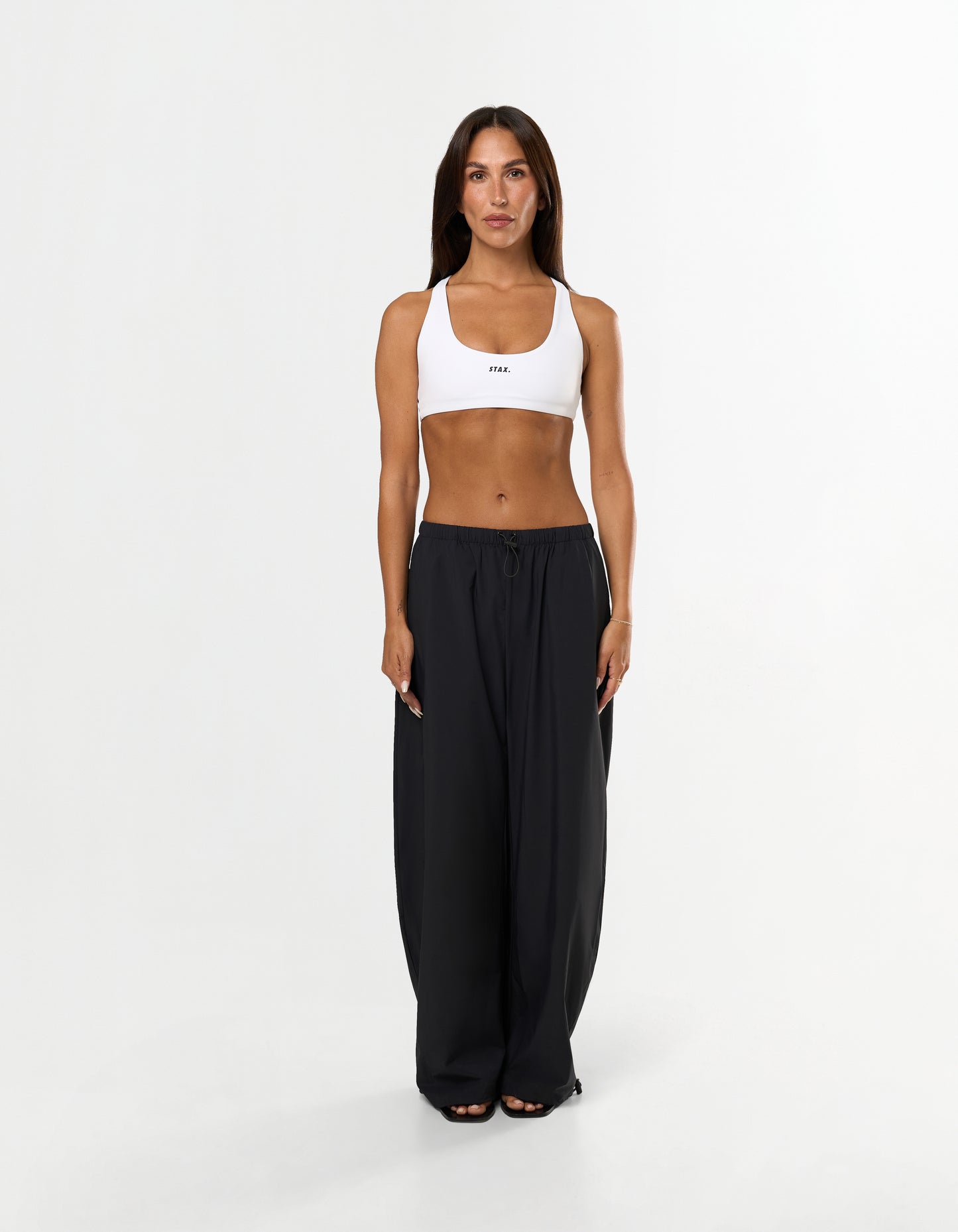 Front view of model wearing STAX. Stella Pants in black showing Toggle drawcord on leg opening and white sports bra