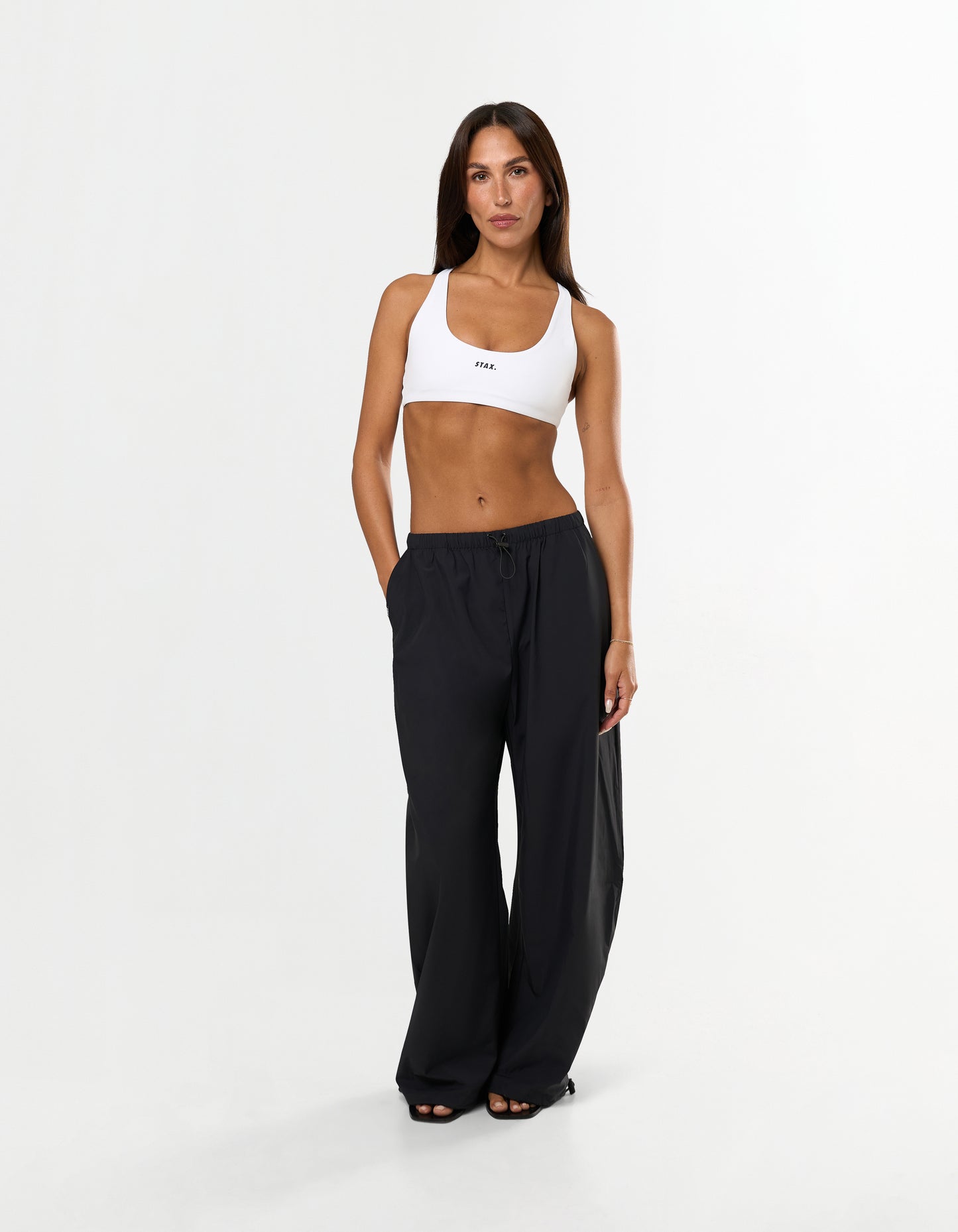 Front view of model wearing STAX. Stella Pants in black with white STAX. Sports bra with black logo
