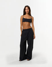 Front view of model wearing STAX. Gigi Pants in black showing outer elastic waistband design and relaxed straight leg fit and black sports bra