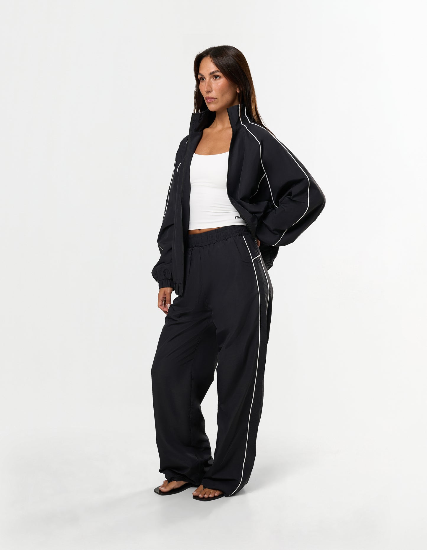 Front view of model wearing STAX. Woven Track Pants in black with open woven track jacket with contrast piping