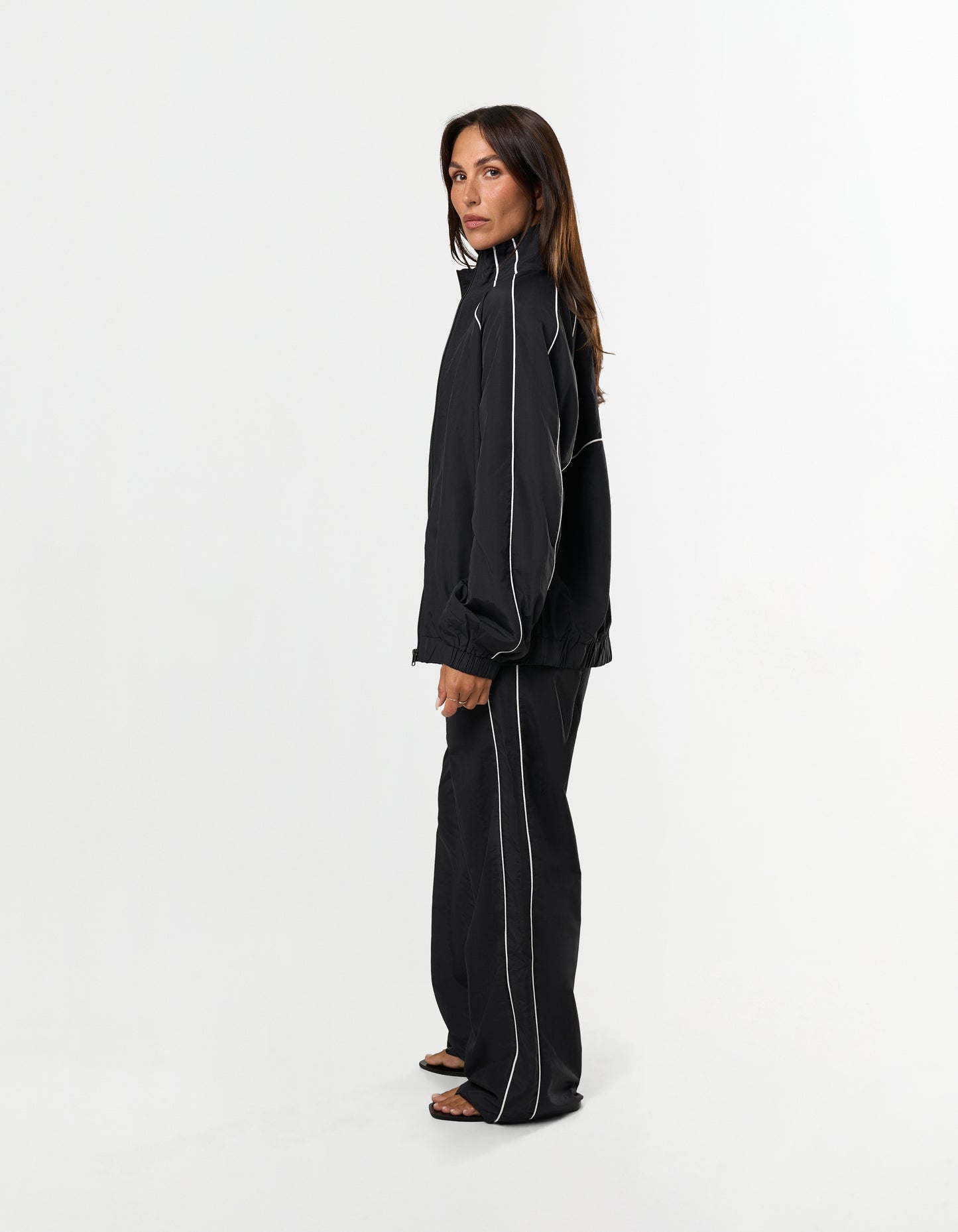 Side profile of STAX. Woven Track Pants in black showing contrast piping detail