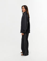 Side profile of STAX. Woven Track Pants in black showing contrast piping detail