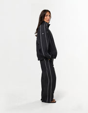 Side profile of STAX. Woven Track Pants and Track Jacket with contrast panelling and white logo detail and slouched fit
