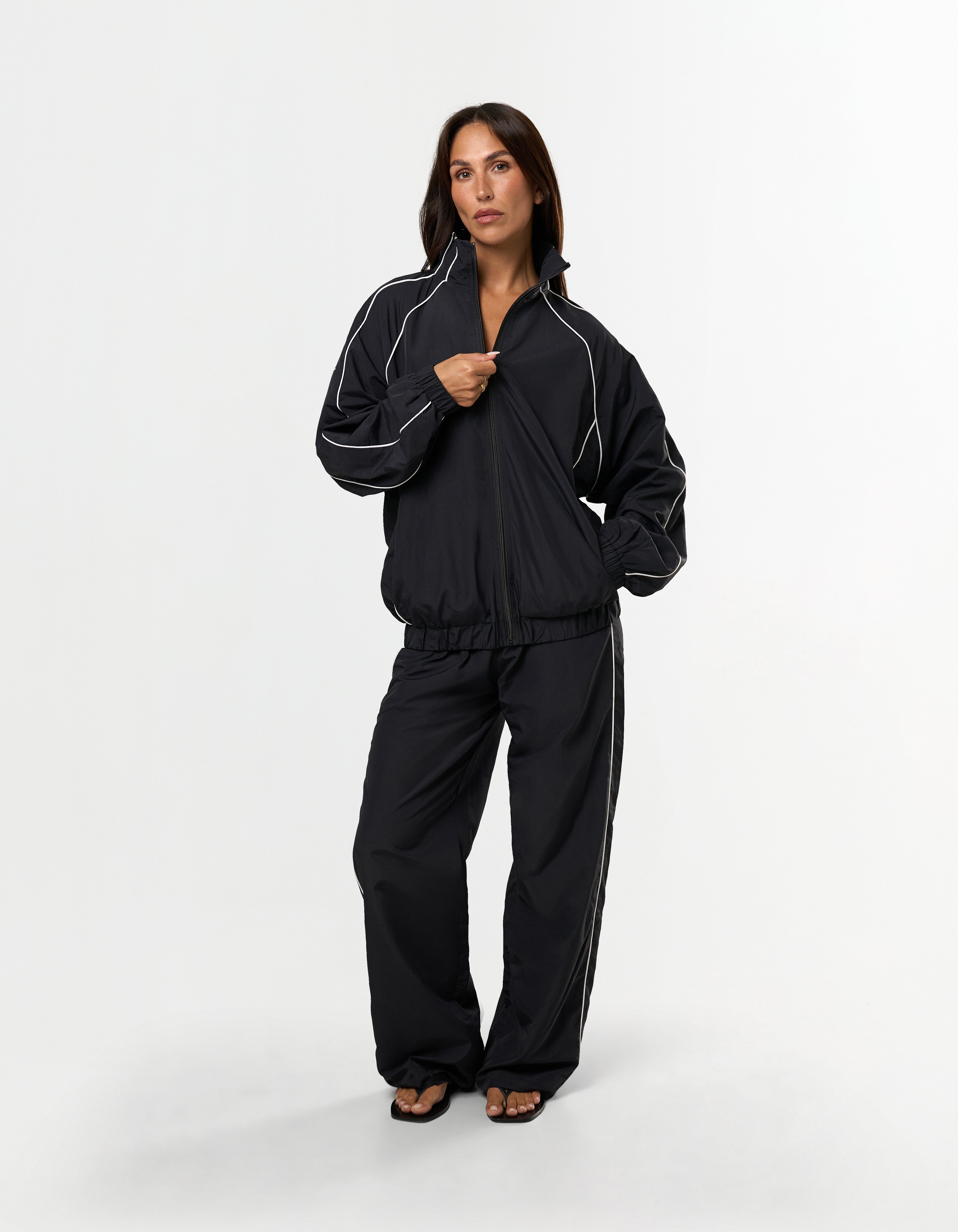Front view of model wearing STAX. Woven Track Jacket zipped up with matching track pants