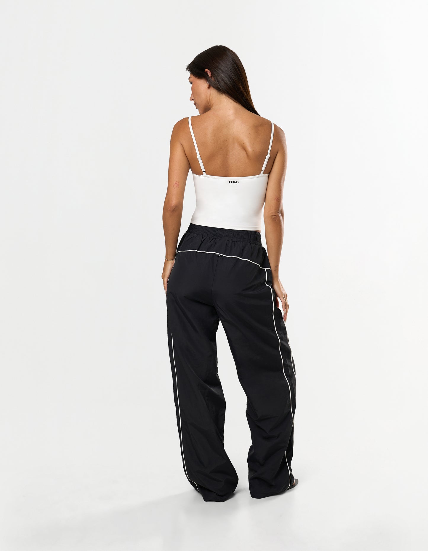 Back view of model wearing STAX. Woven Track Pants in Black with white sculpt tank