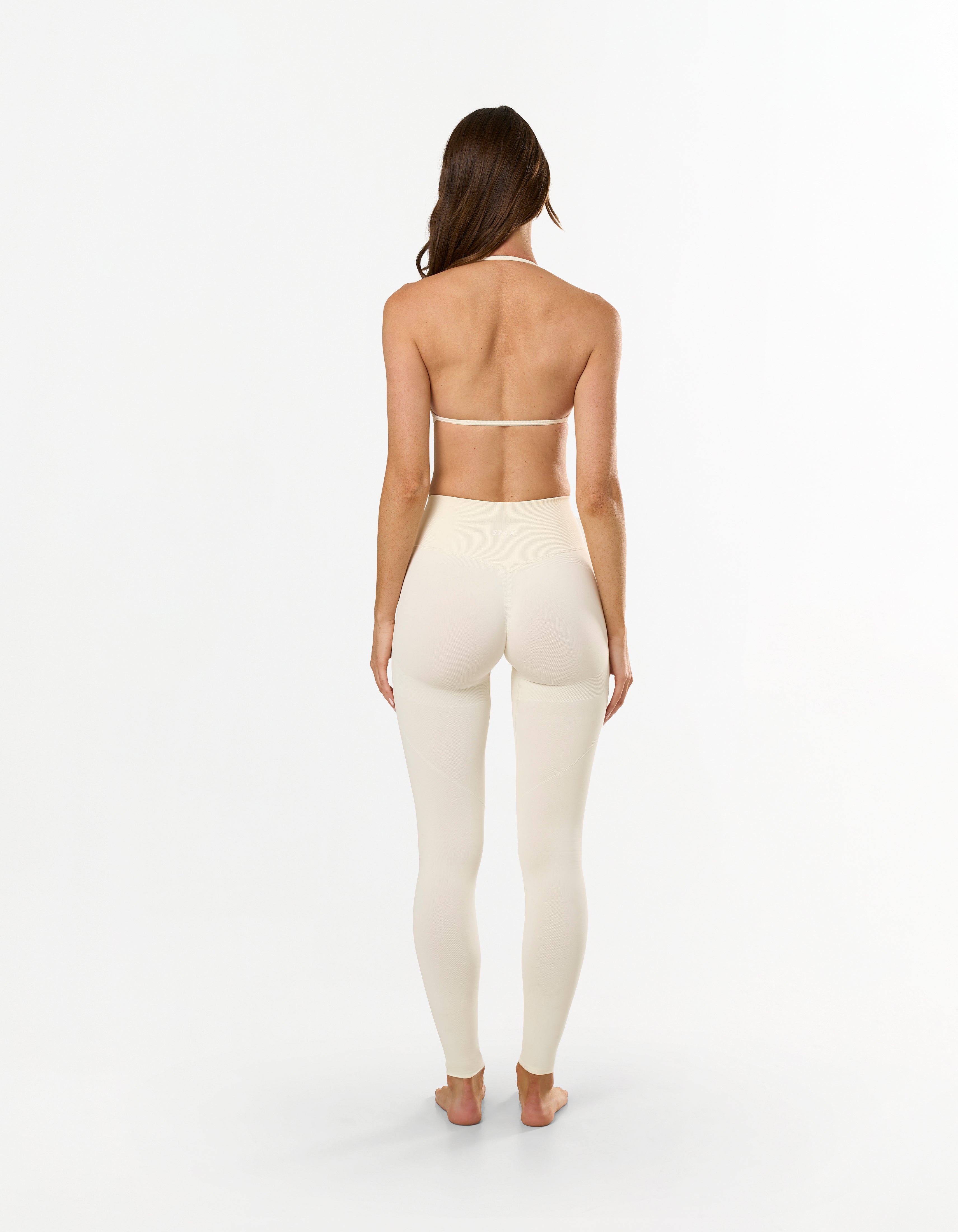 Back profile of model wearing STAX. Premium Seamless Skulpt Leggings in Cream with V back glute contouring seam
