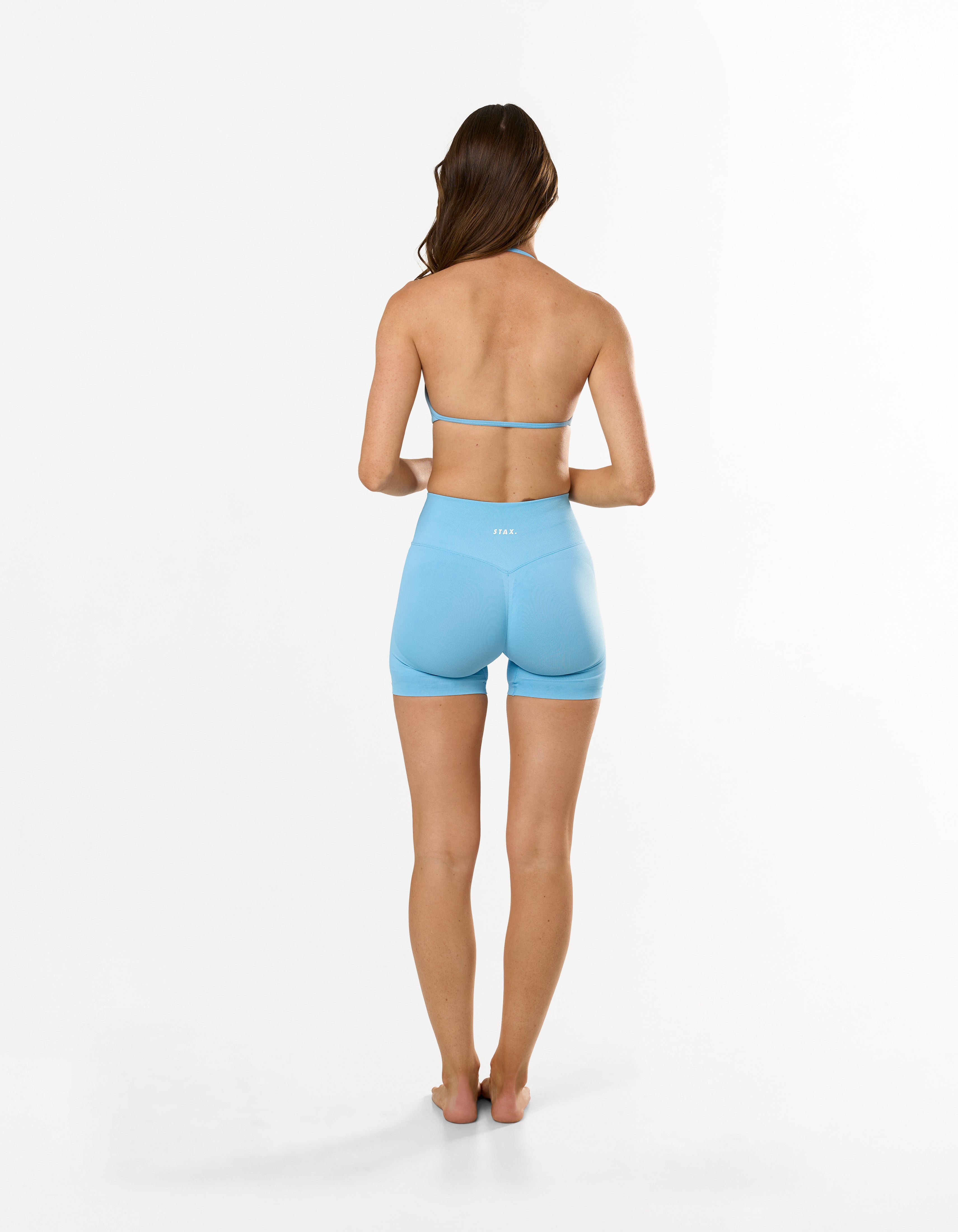 Back view of model wearing Premium Seamless Skulpt Midi Bike Shorts in Blue showing V back glute contouring seam and Invisible contouring scrunch