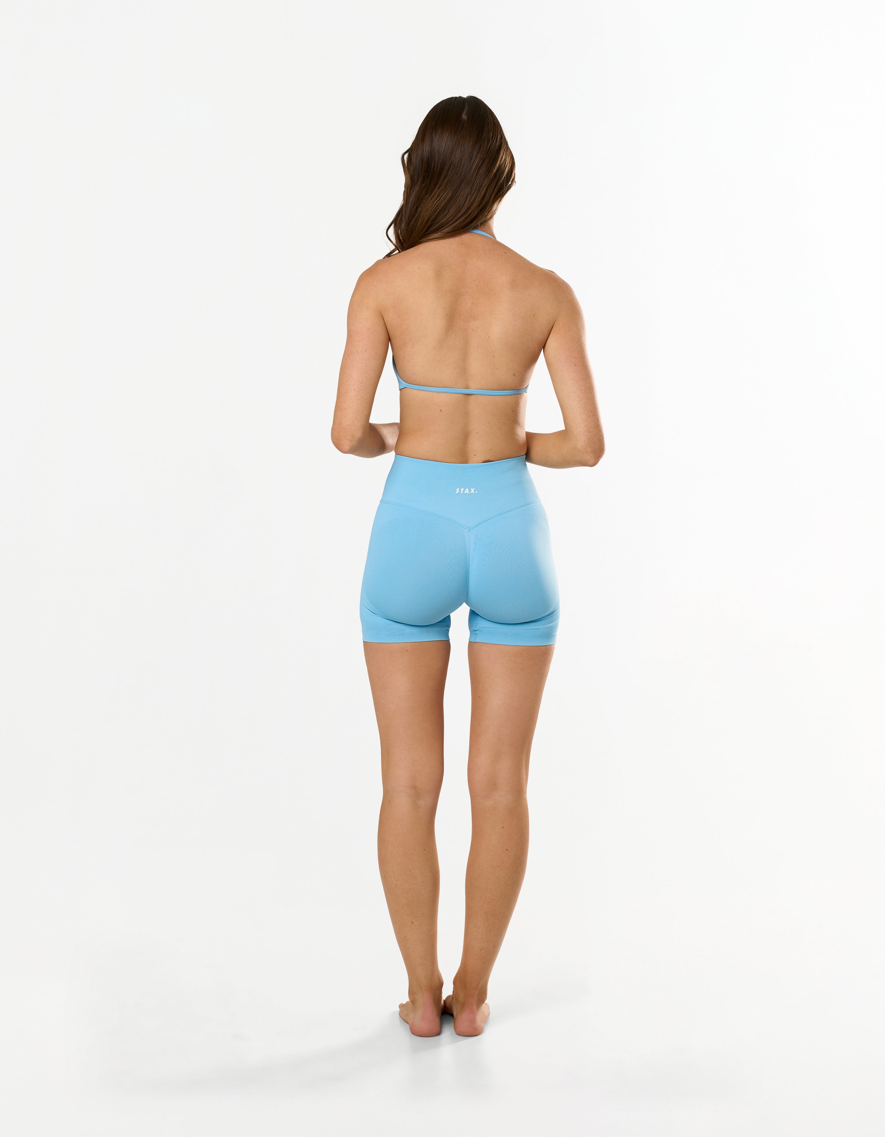 Back view of model wearing Premium Seamless Skulpt Midi Bike Shorts in Blue showing V back glute contouring seam and Invisible contouring scrunch