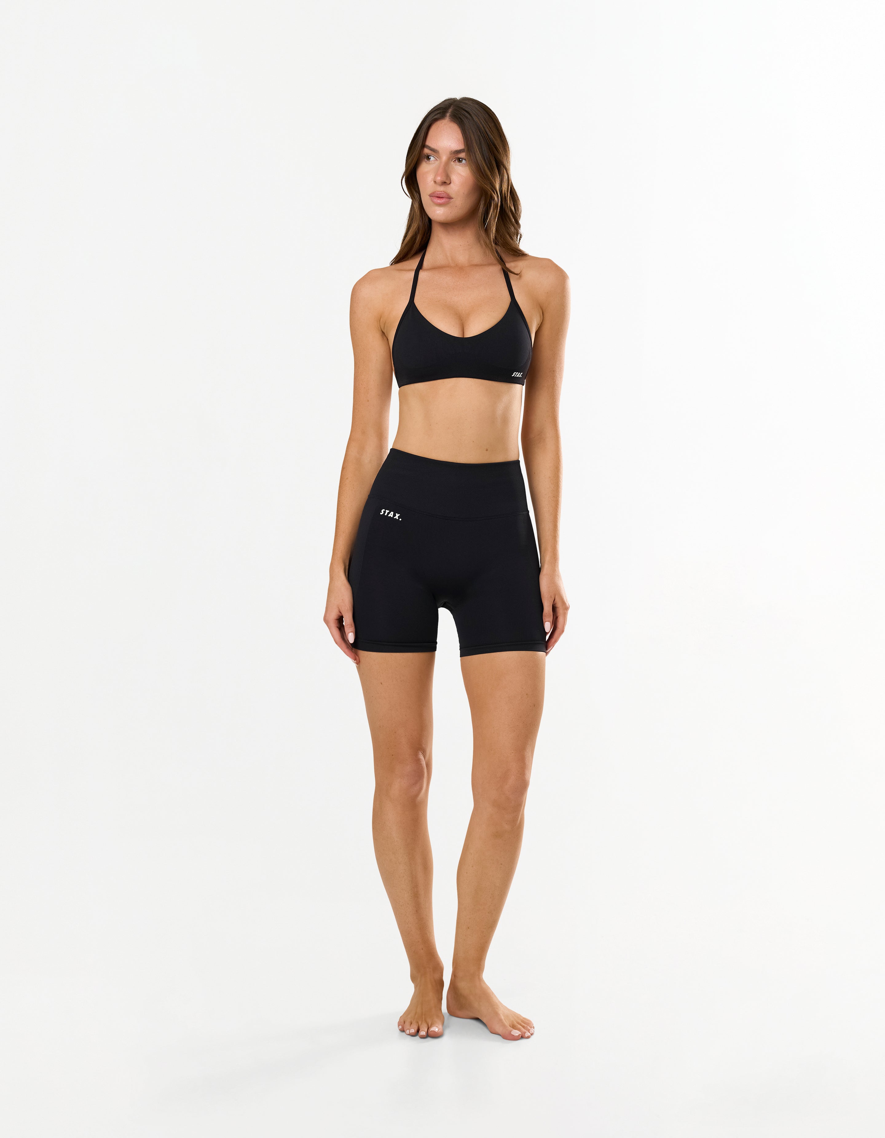Front profile of model wearing STAX. Premium Seamless Skulpt Midi Bike Shorts   in Black showing flattering compressive ribbed waistband