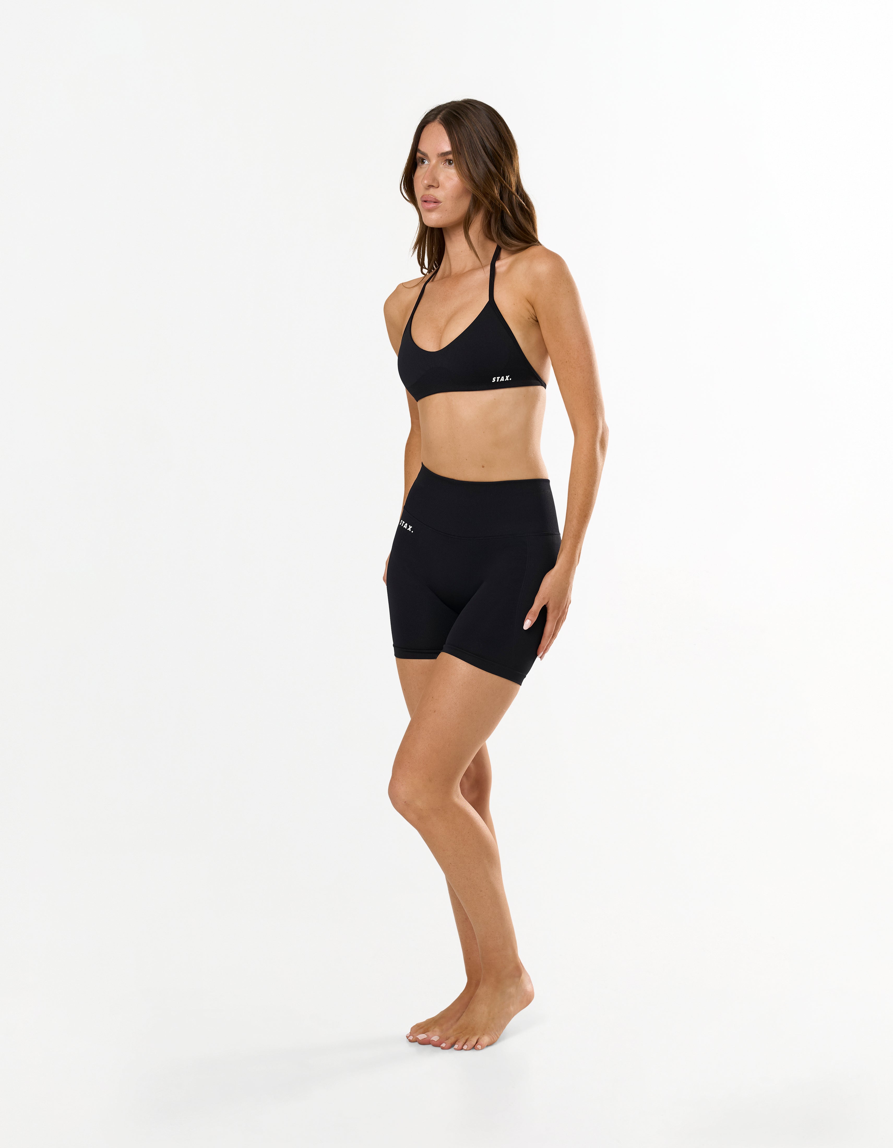 Front profile of model wearing STAX. Premium Seamless Skulpt Midi Bike Shorts   in Black showing flattering compressive fit