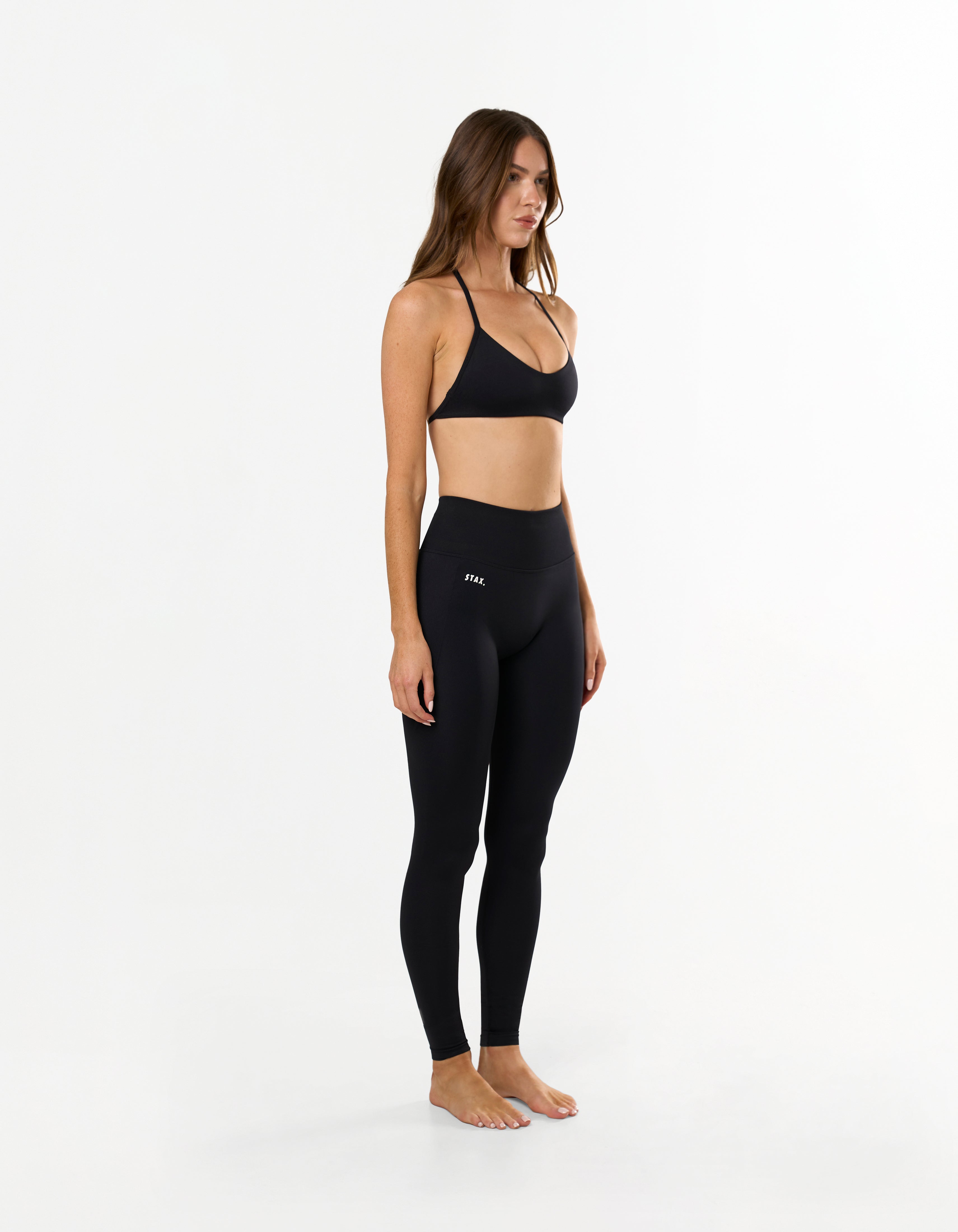 Side view of model wearing STAX. Premium Seamless Skulpt Bralette in Black with matching Premium Seamless Skulpt Full Length Tights
