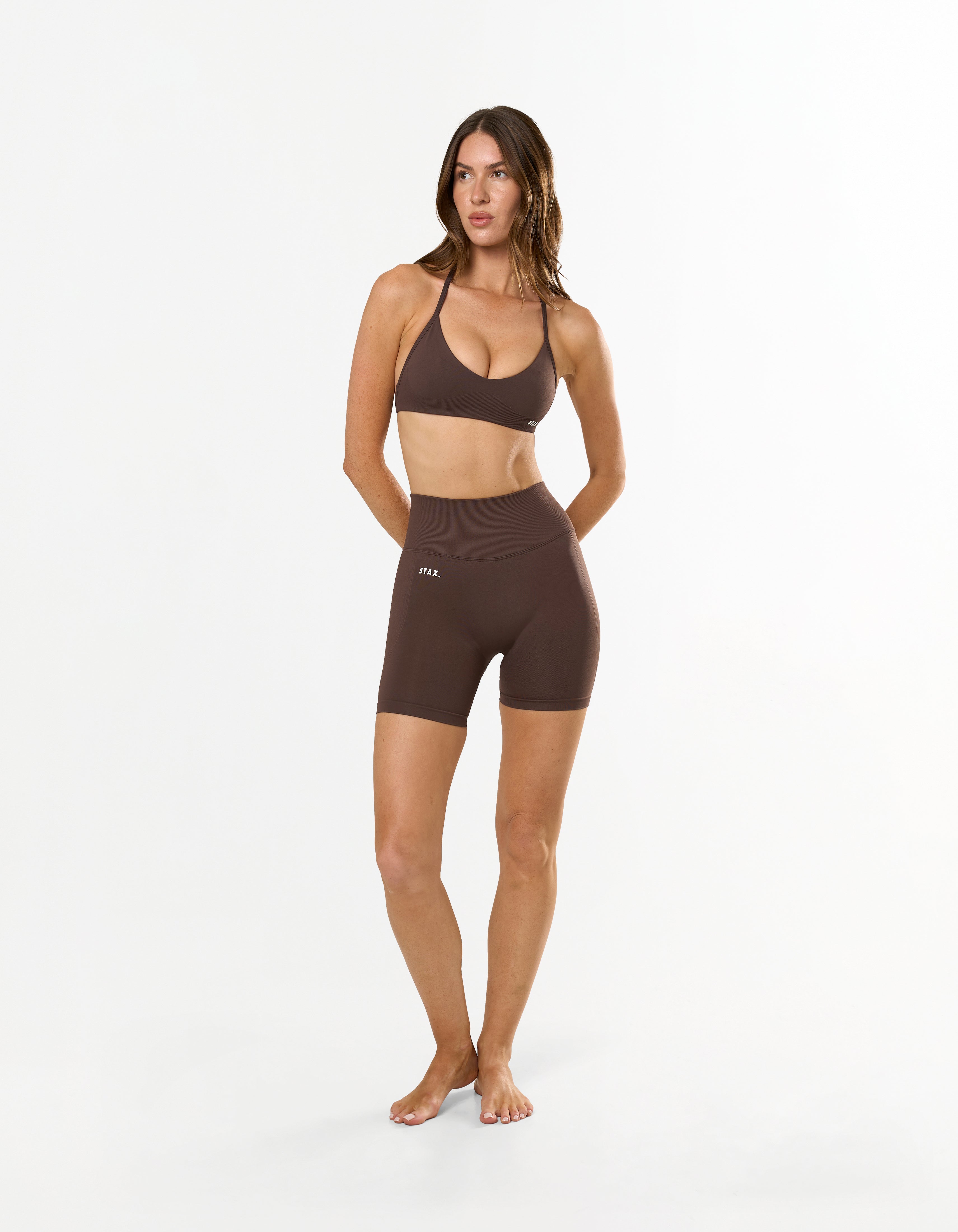 Front profile of model wearing STAX. Premium Seamless Skulpt Midi Bike Shorts in Brown with matching skulpt halter bralette in brown