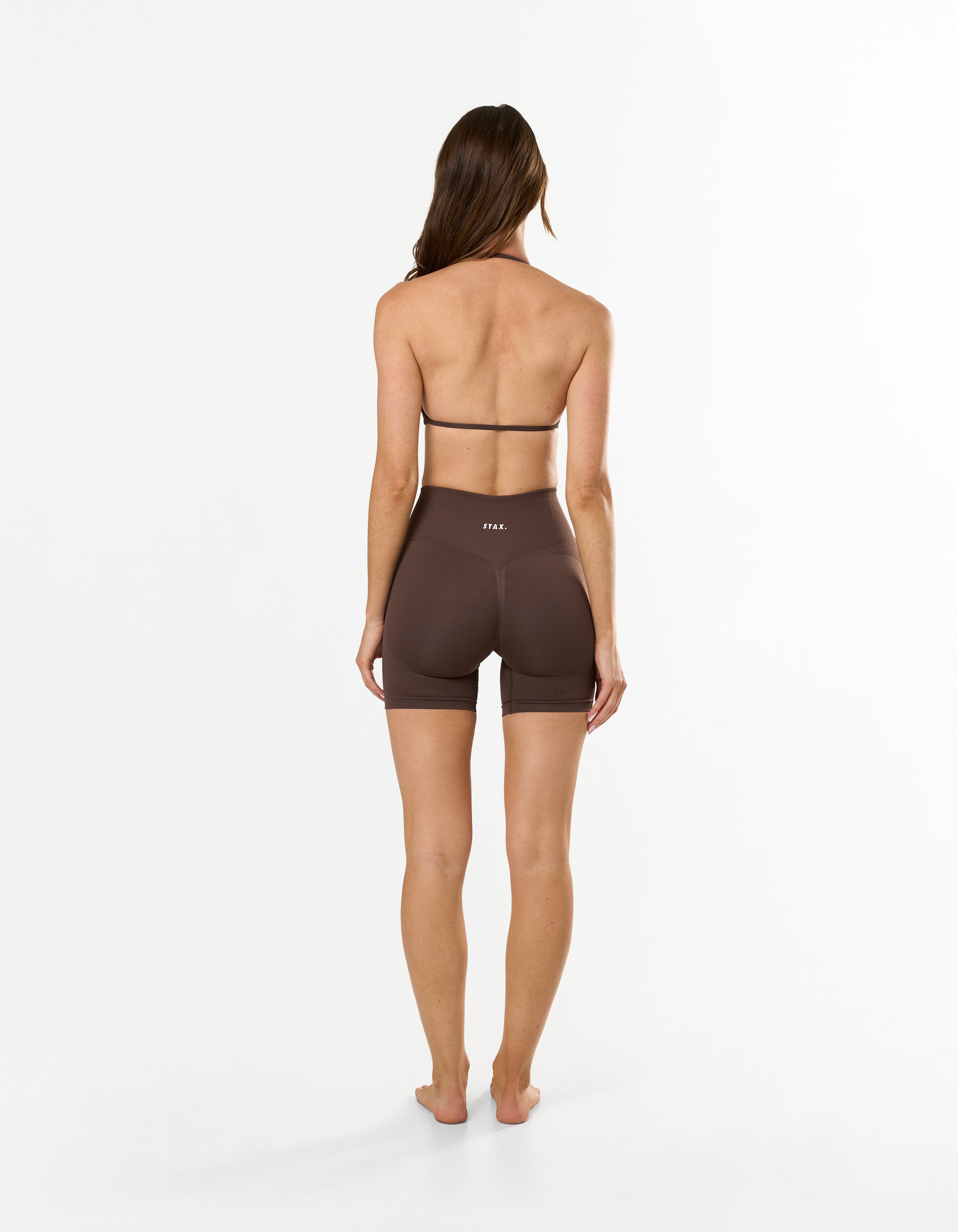 Back view of model wearing STAX. Premium Seamless Skulpt Midi Bike Shorts in Brown showing V back glute contouring seam