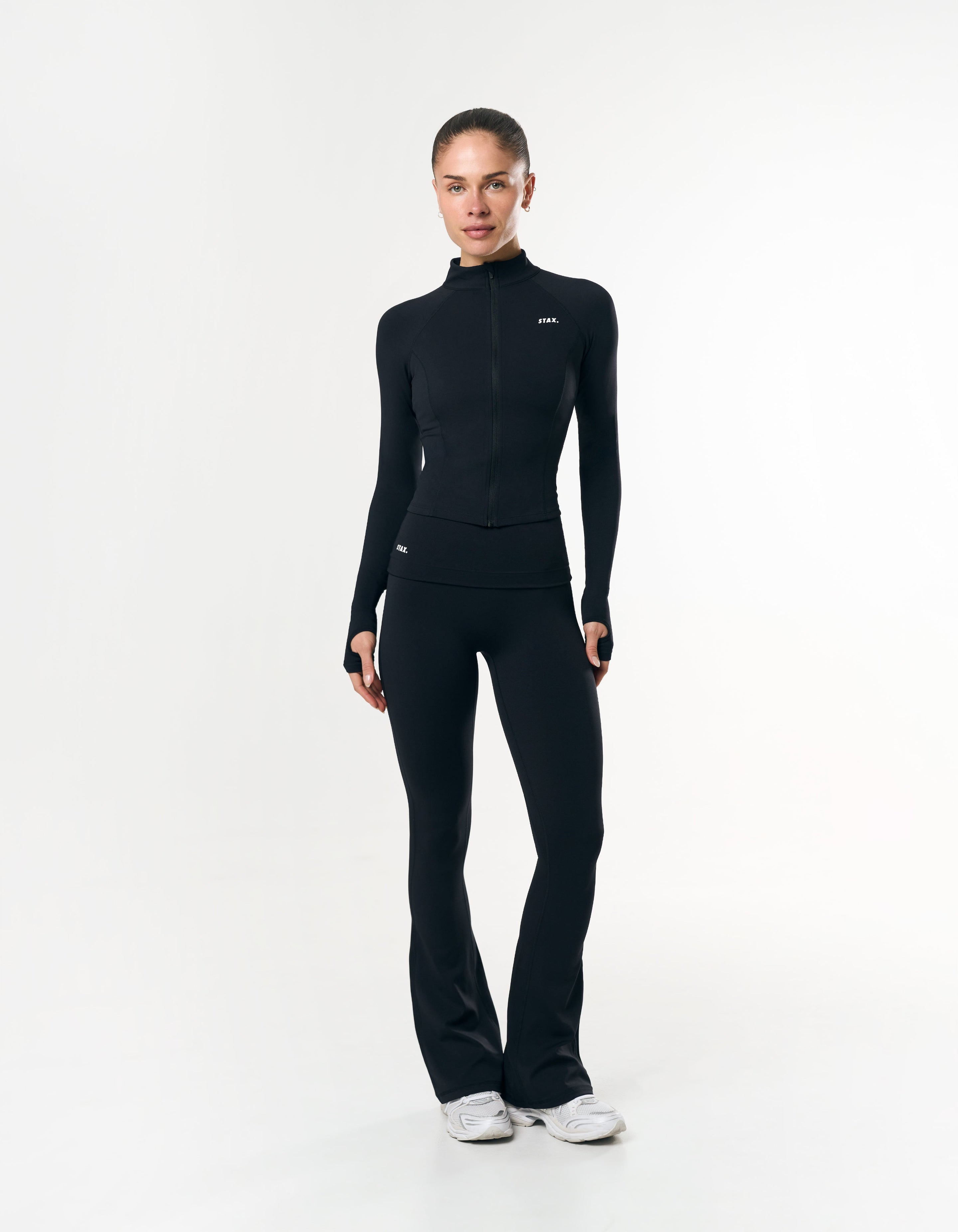Front view of model wearing STAX. Fold over flares in airlyte material with matching zip jacket with thumb loops