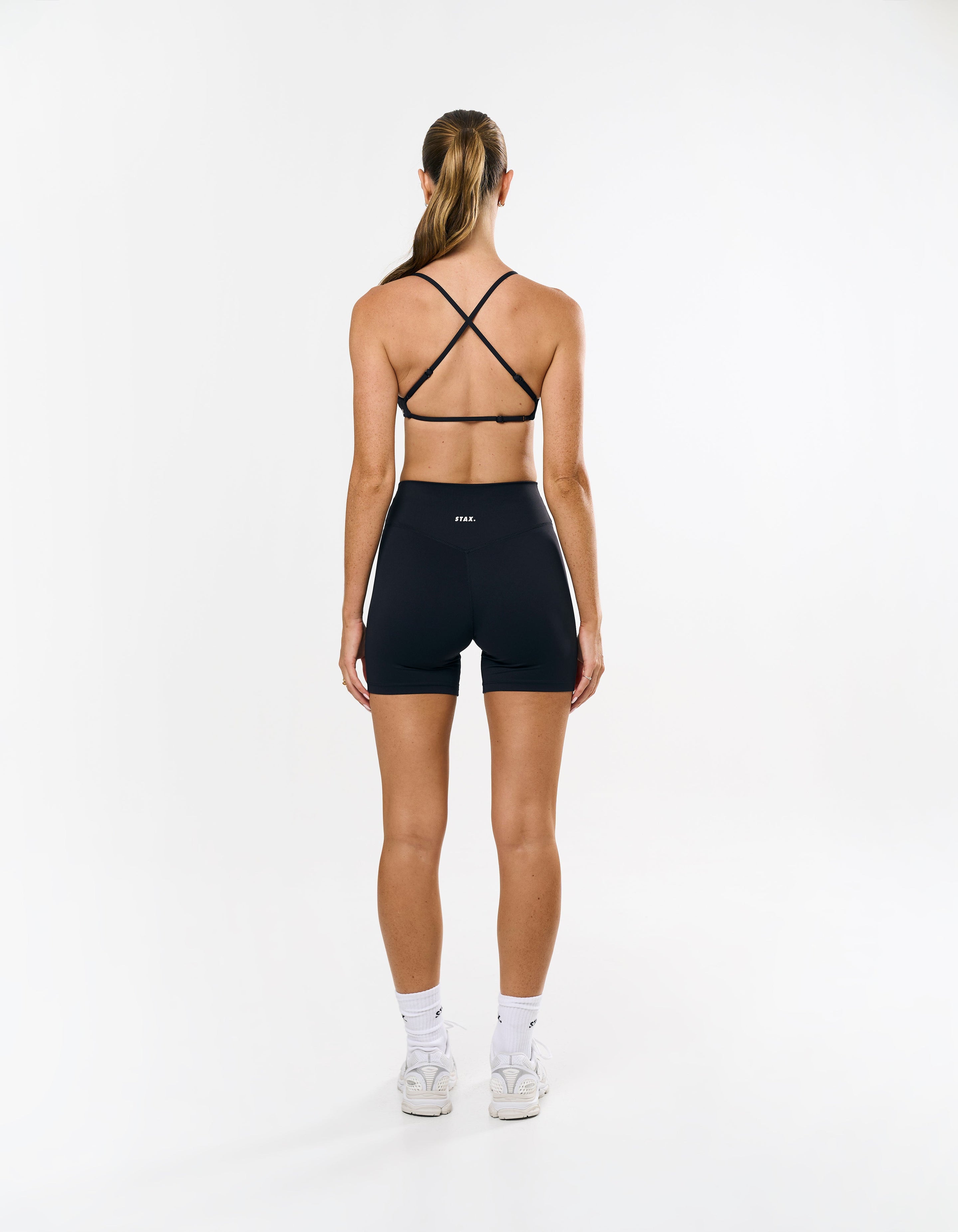 Back view of STAX. Midi Bike Shorts Airlyte in Black with matching sports bra showing cross back design 